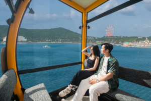 Cặp đôi ngồi trong cabin cáp treo ngắm biển và vòng quay tại Vinpearl Harbour – giá vinpearl harhour nha trang và trải nghiệm thực tế khi tham quan