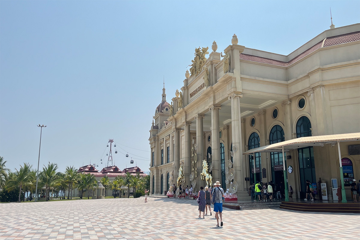 Du khách tham quan khu vực cổng vào VinWonders Nha Trang với kiến trúc châu Âu sang trọng, phía xa là tuyến cáp treo vượt biển nổi tiếng. 