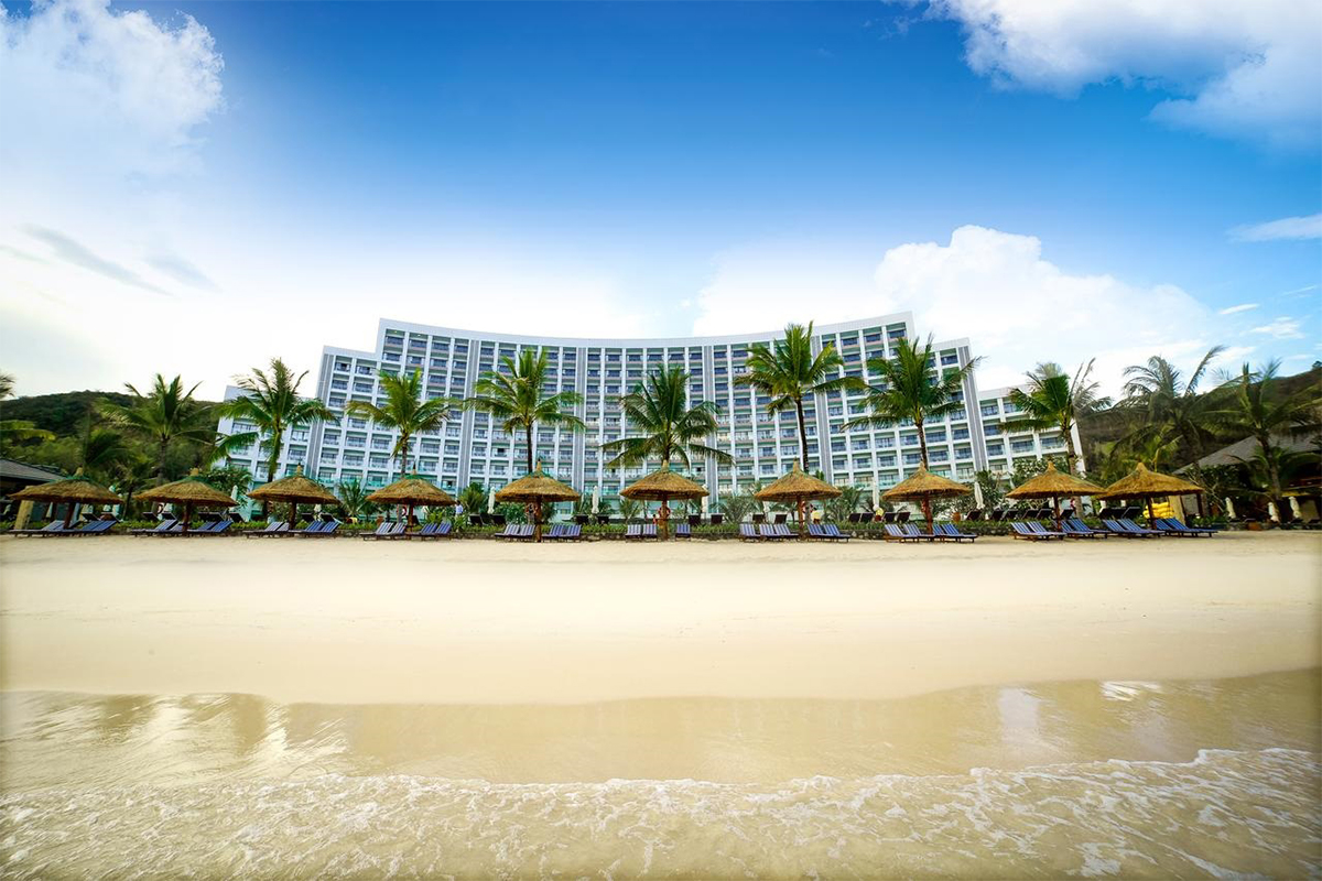 Khách sạn vinpearl nha trang bay nhìn từ bãi biển với hàng dừa, ô che nắng và không gian nghỉ dưỡng sang trọng