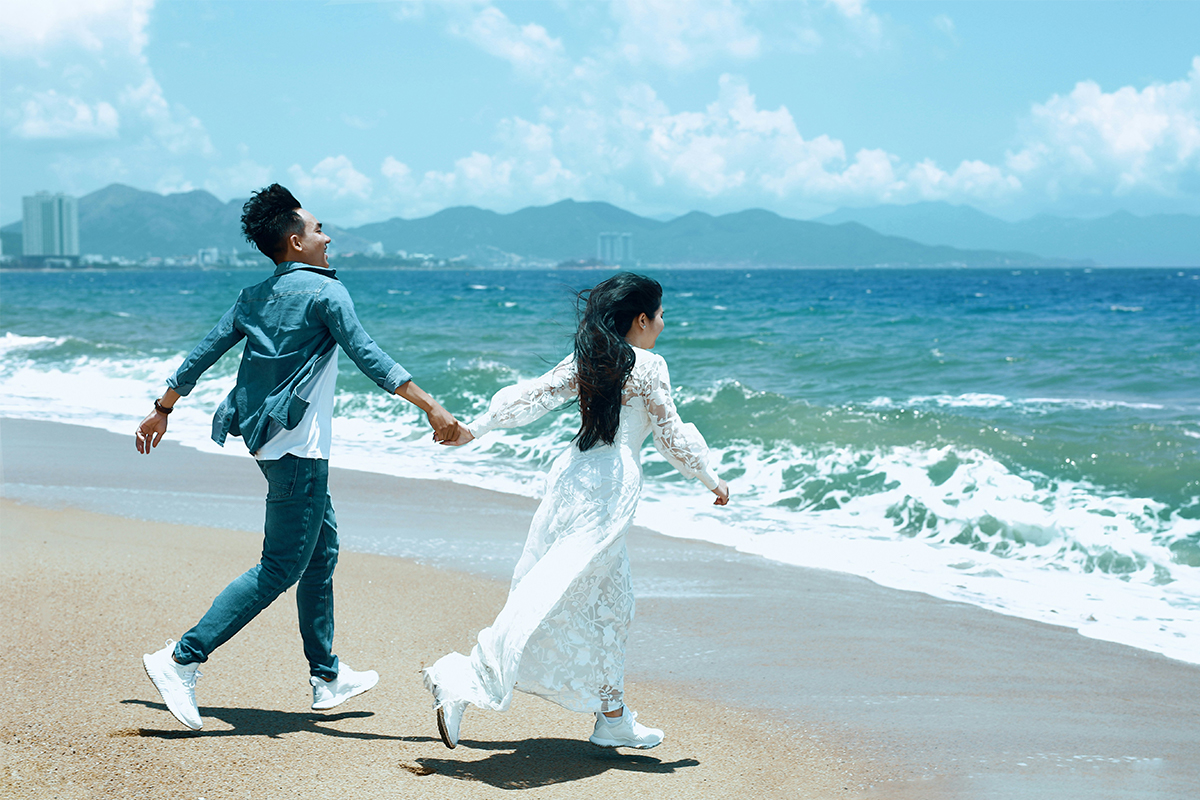 Cặp đôi nắm tay chạy trên bãi biển Nha Trang trong chuyến nghỉ dưỡng và đi chơi lãng mạn.