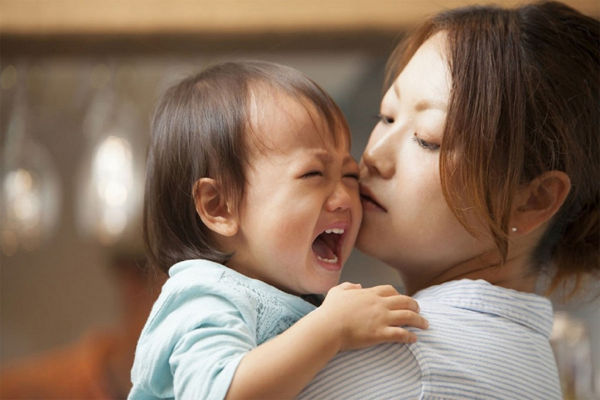 Khoảnh khắc gia đình ấm áp khi người mẹ ôm và vỗ về em bé đang khóc, thể hiện tình yêu thương và sự chăm sóc.