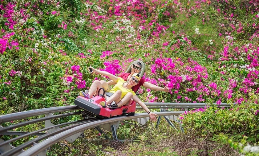 Hai du khách đi xe trượt núi qua những bụi hoa giấy tại VinWonders Nha Trang