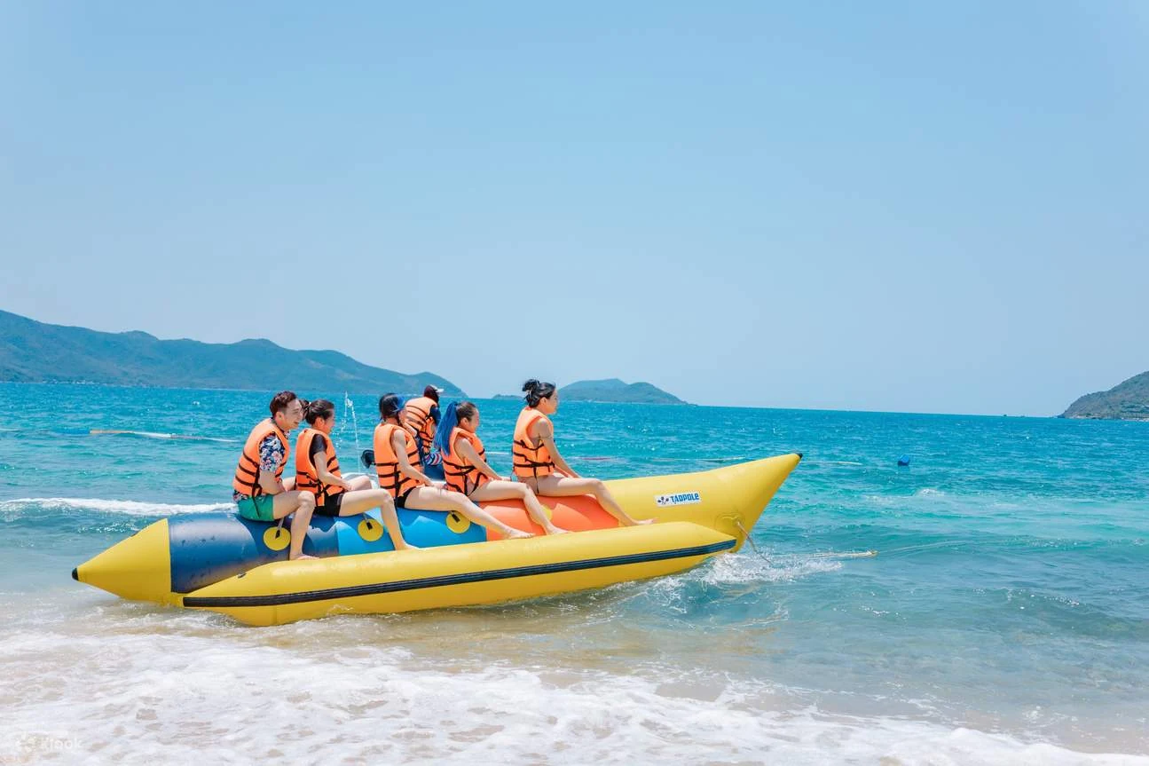 Nhóm du khách mặc áo phao ngồi trên phao chuối màu vàng ngoài biển